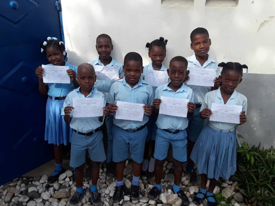 Eight students in blue uniforms holding report cards in front of a blue door